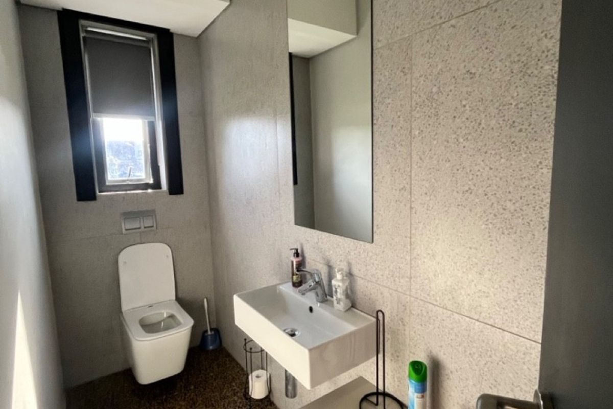 Modern industrial-style bathroom featuring a wall-mounted toilet, floating vanity with basin, large wall mirror, and contemporary grey tiled finishes.