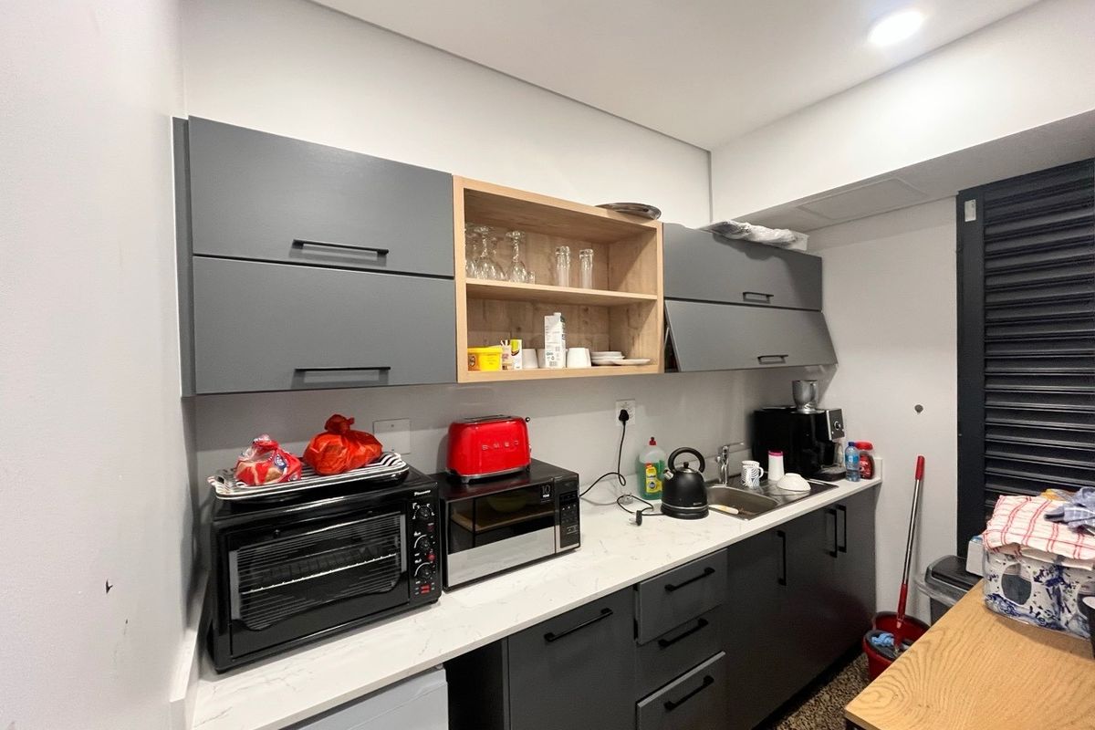 A compact, modern kitchen area featuring dark grey cabinetry, light stone-look countertops, and an integrated sink, providing efficient workspace for industrial or office use.