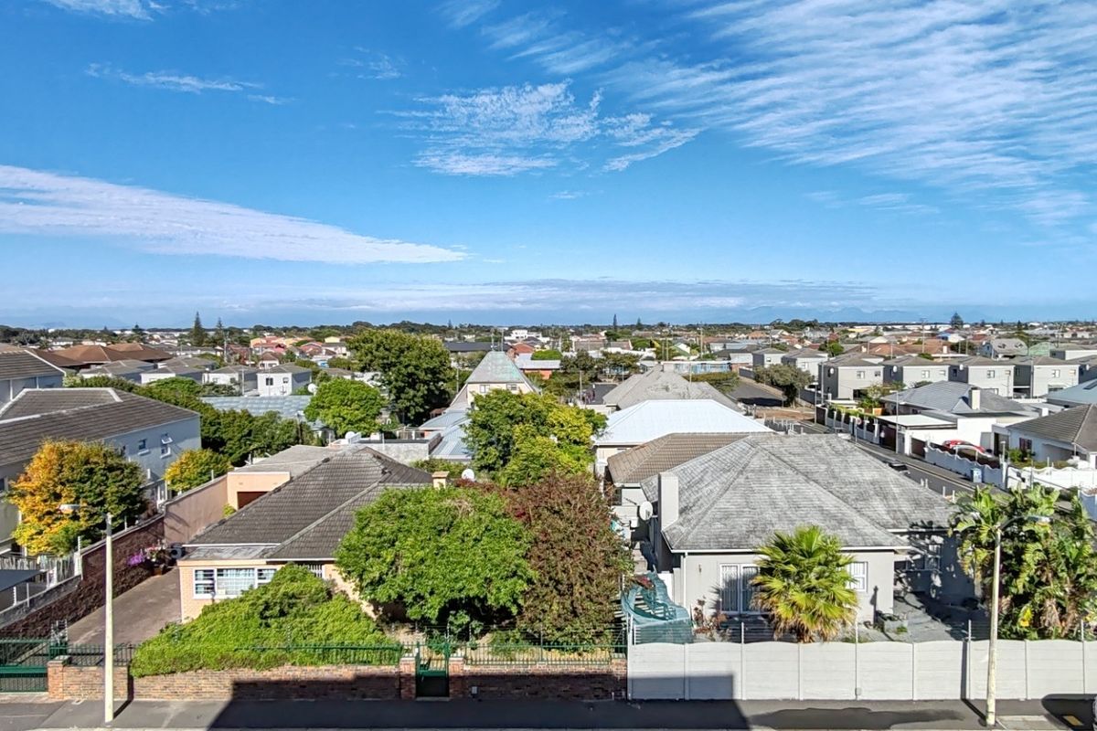 An elevated view overlooking a suburban residential neighborhood with various houses, mature trees, and clear blue skies.