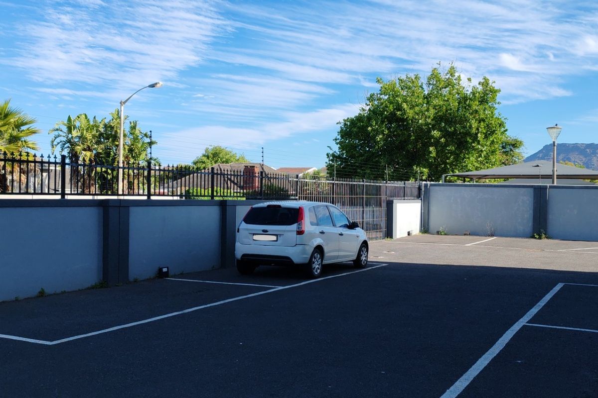 A paved outdoor parking area featuring perimeter boundary walls with integrated security fencing and street lighting.