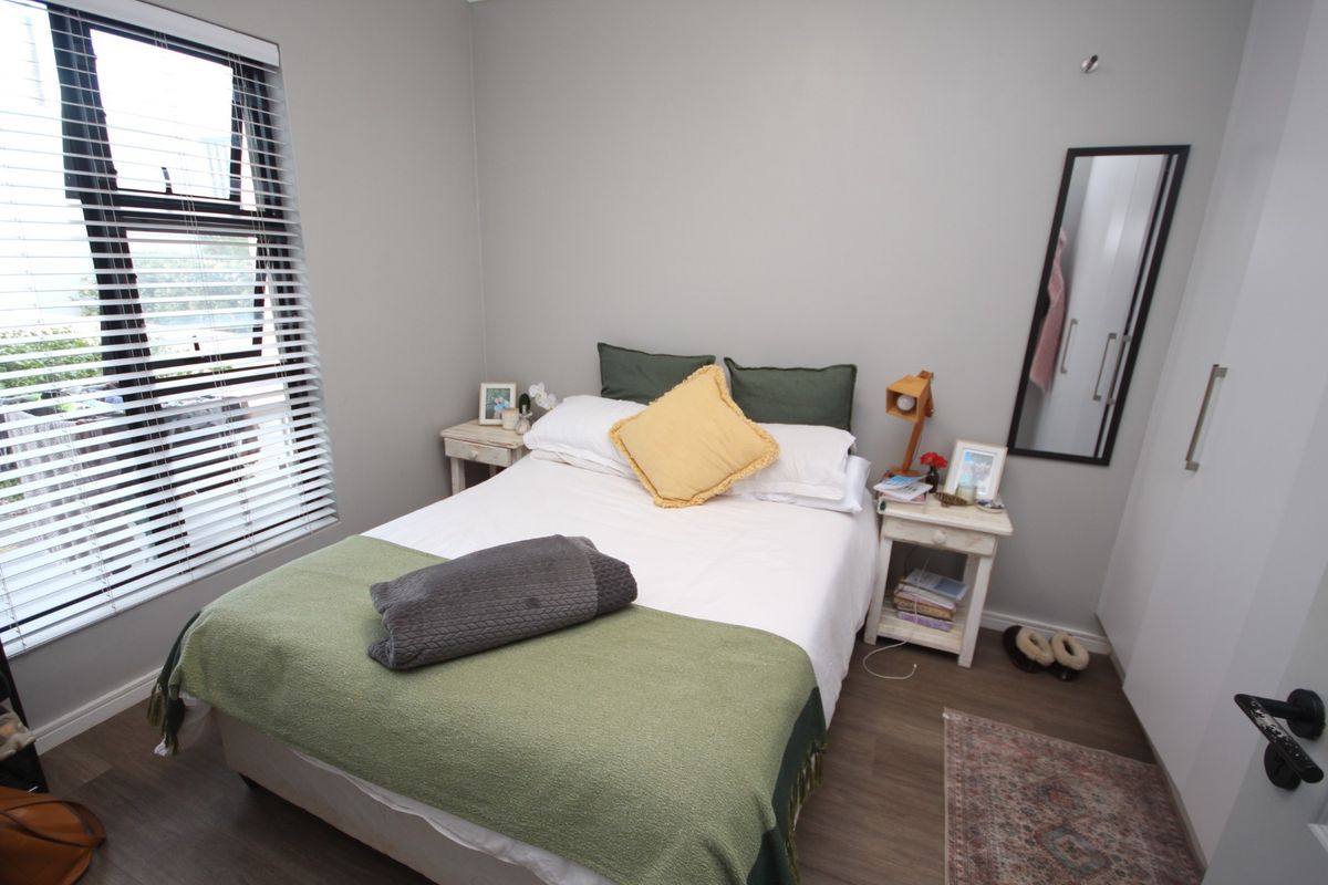 A well-maintained bedroom featuring modern laminate flooring, built-in cupboards, and a large window with fitted blinds.