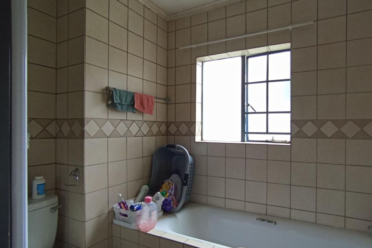 A functional bathroom featuring a built-in bathtub, tiled walls with decorative accents, and a window providing natural light.