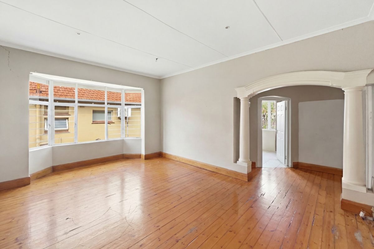 Spacious living area featuring polished timber flooring, a large bay window, and a decorative arched entryway with classic columns.