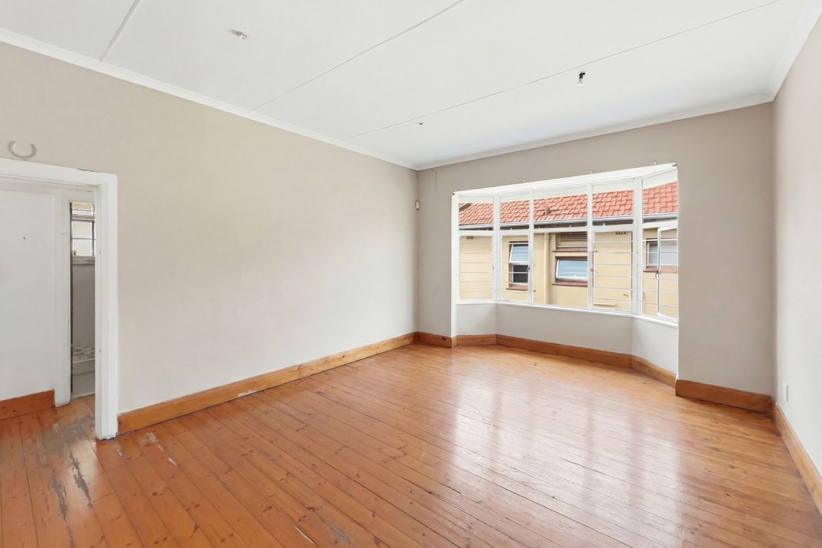 A spacious, empty bedroom featuring original timber flooring, neutral wall tones, and a large bay window providing natural light.
