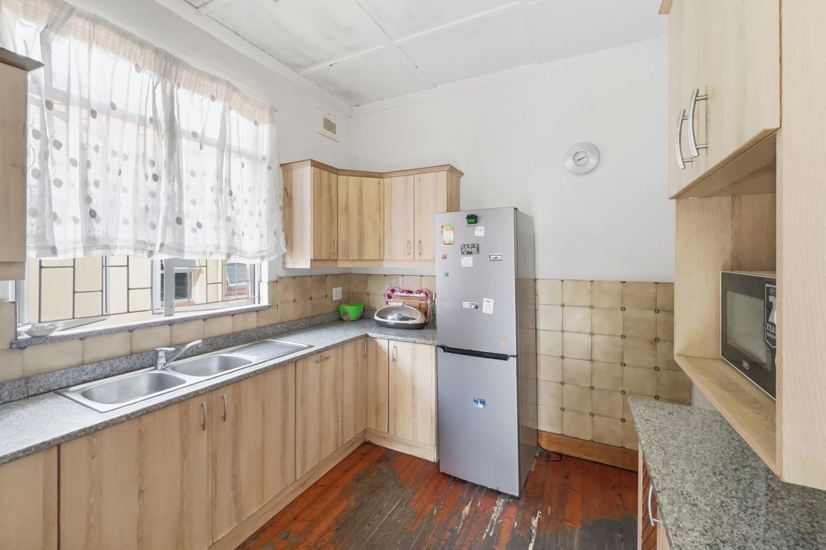 A functional kitchen featuring light wood cabinetry, granite-look countertops, a double stainless steel sink, and original wooden flooring.
