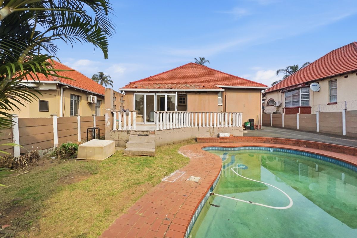 Rear view of the property featuring a swimming pool, brick paved surround, and a raised patio area with balustrade access to the main house.