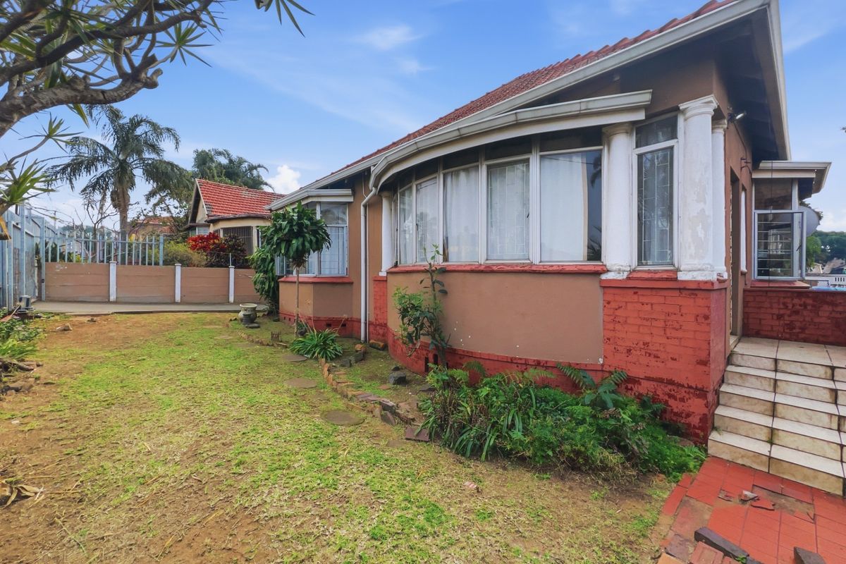 Exterior view of the house featuring a curved facade, classic columns, and a surrounding garden area with tiled entrance steps.