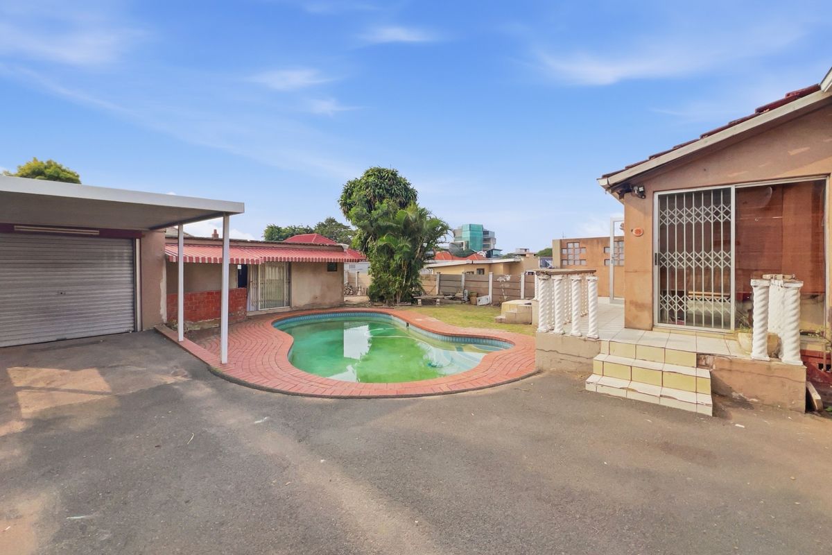 Rear exterior view featuring a swimming pool, paved surround, covered carport, and a raised patio area with balustrades.