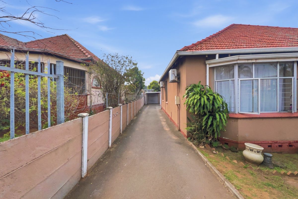 A paved driveway leading to a rear garage, flanked by a residential building with a tiled roof and a boundary wall.