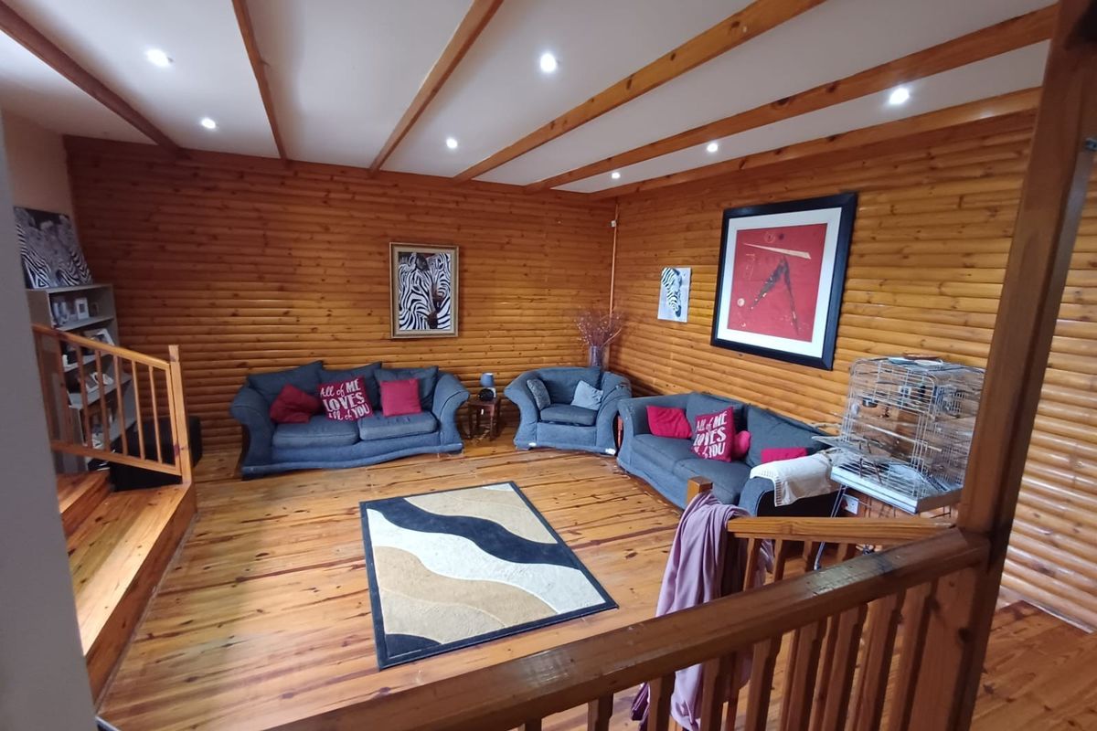 Spacious living area featuring warm timber wall paneling, exposed wooden ceiling beams, and polished wooden flooring with a mezzanine level staircase.