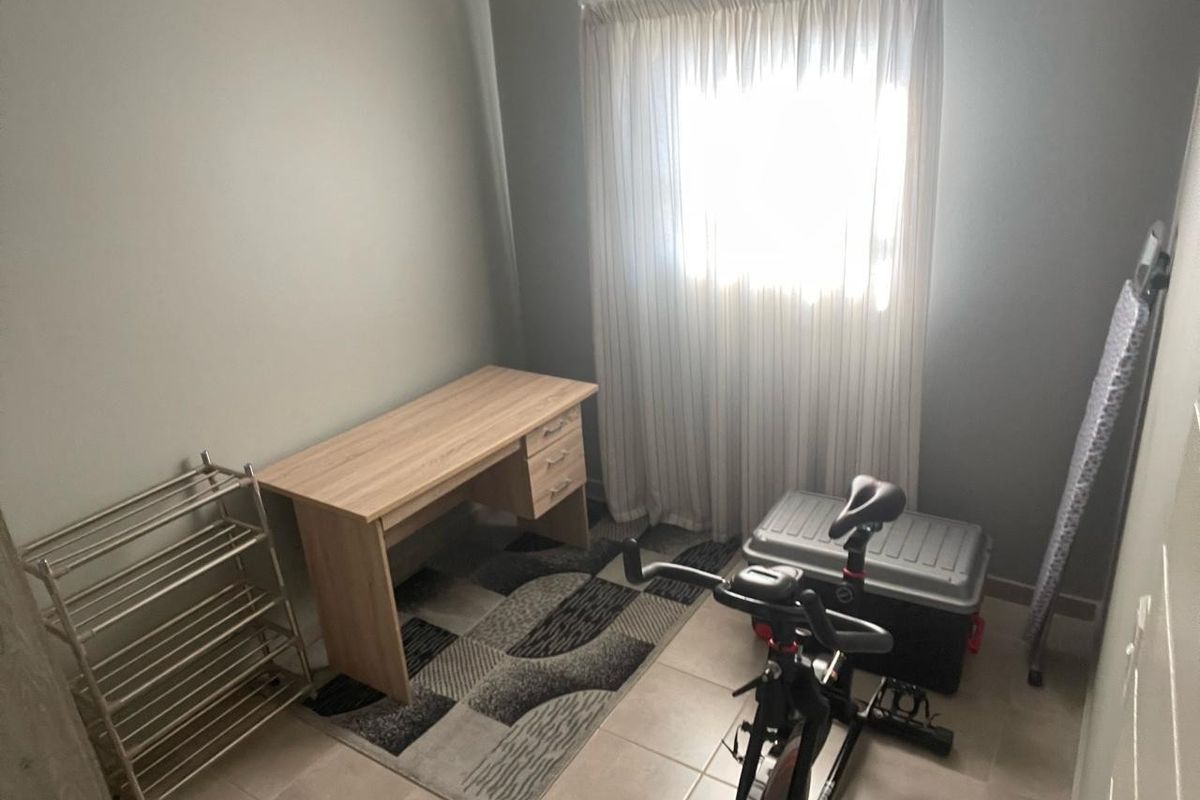 A functional bedroom or office space featuring tiled flooring and a window with curtains, suitable for various uses.