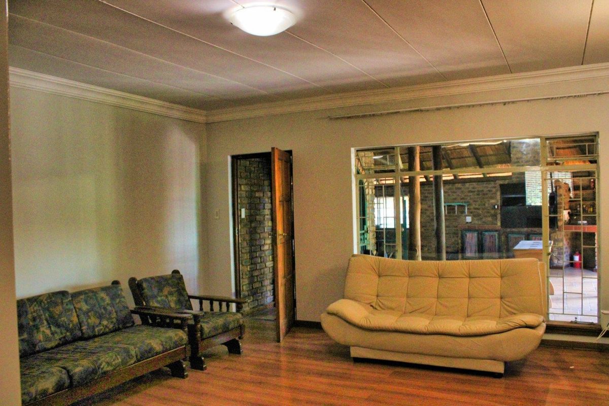 A living room featuring laminate flooring, ceiling tiles, and a large window looking out towards an outdoor area.