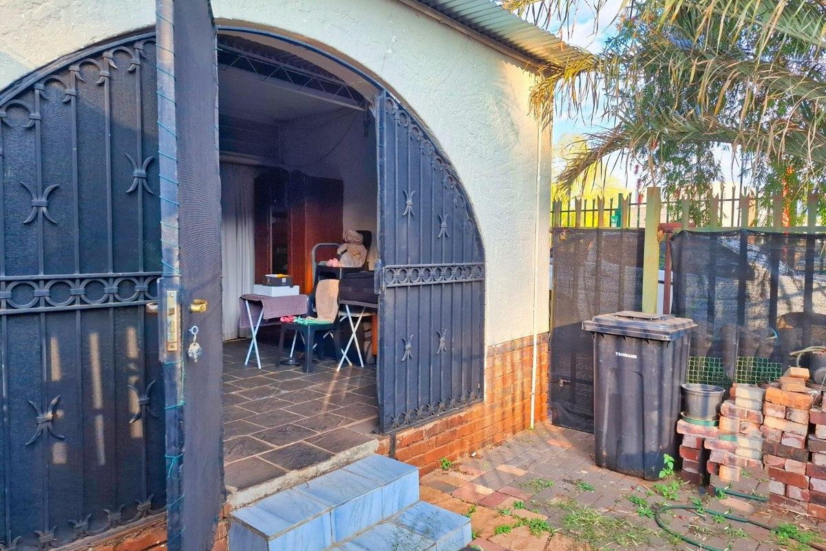 Rear exterior view of an apartment featuring a wrought iron security gate, tiled patio area, and brick foundation with visible signs of weathering.