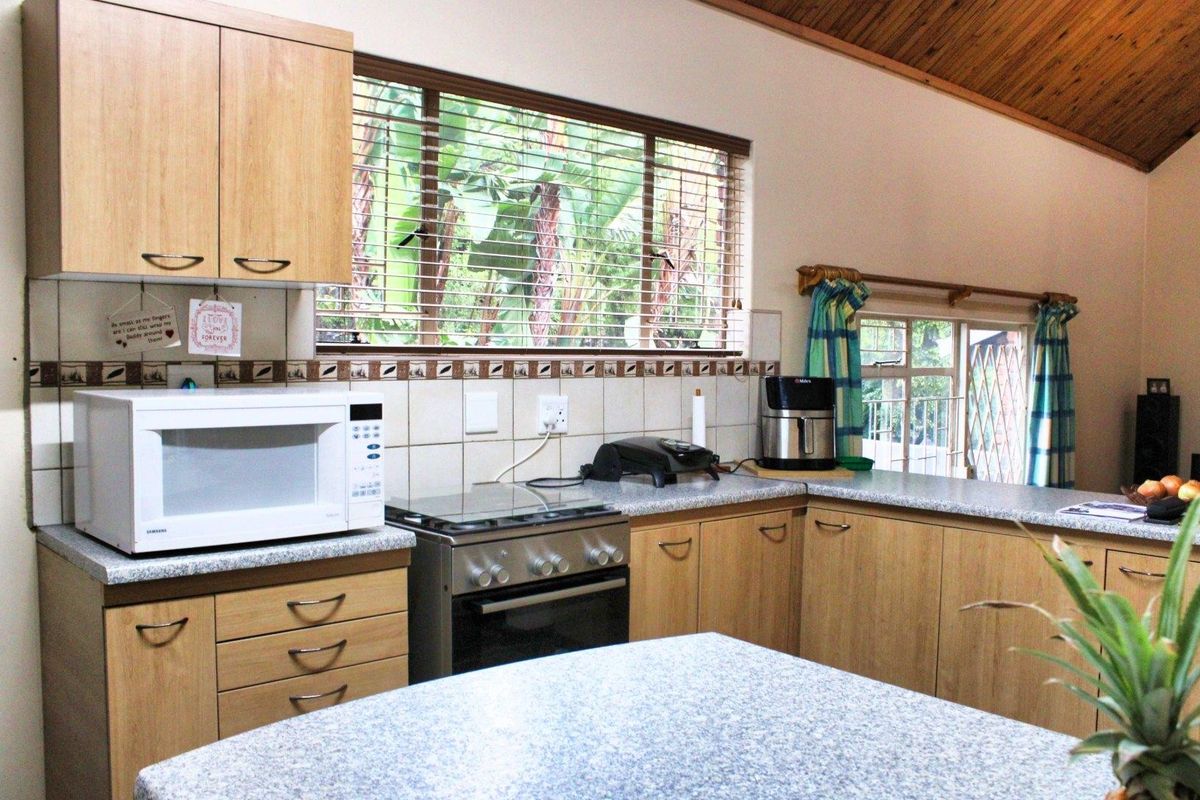 A functional kitchen featuring light wood-look cabinetry, granite-style countertops, a freestanding gas stove, and a distinctive timber raked ceiling.