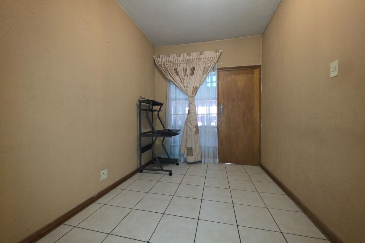 A compact, tiled room featuring a wooden door and window with curtains, suitable for use as a small bedroom or home office space.