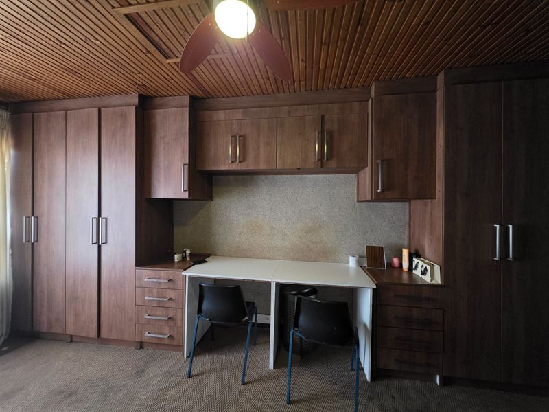 A bedroom featuring extensive built-in dark wood cabinetry, integrated desk space, and a timber-paneled ceiling with a central fan.