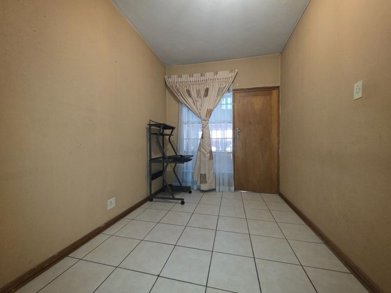 A compact, tiled room featuring a wooden door and window with curtains, suitable for use as a small bedroom or home office space.