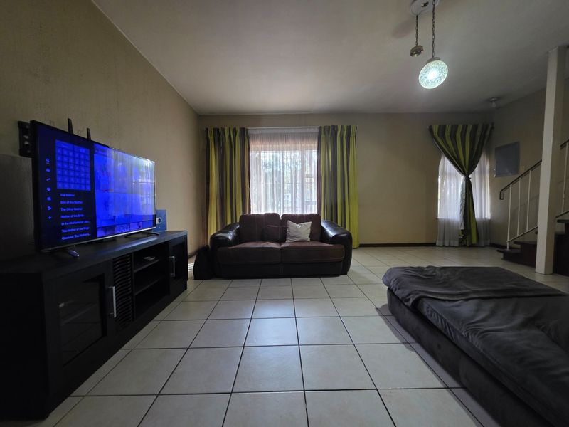 Spacious living room featuring neutral ceramic floor tiles, large windows for natural light, and an open staircase leading to the upper level.