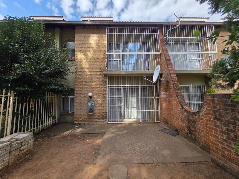 Rear view of a townhouse featuring a paved patio area, brick facade, and security bars on all windows and sliding doors.