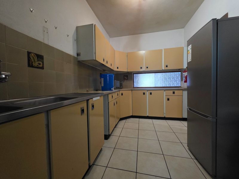 A dated kitchen featuring original cabinetry, tiled flooring, and a stainless steel sink, offering a functional layout ready for modernization.