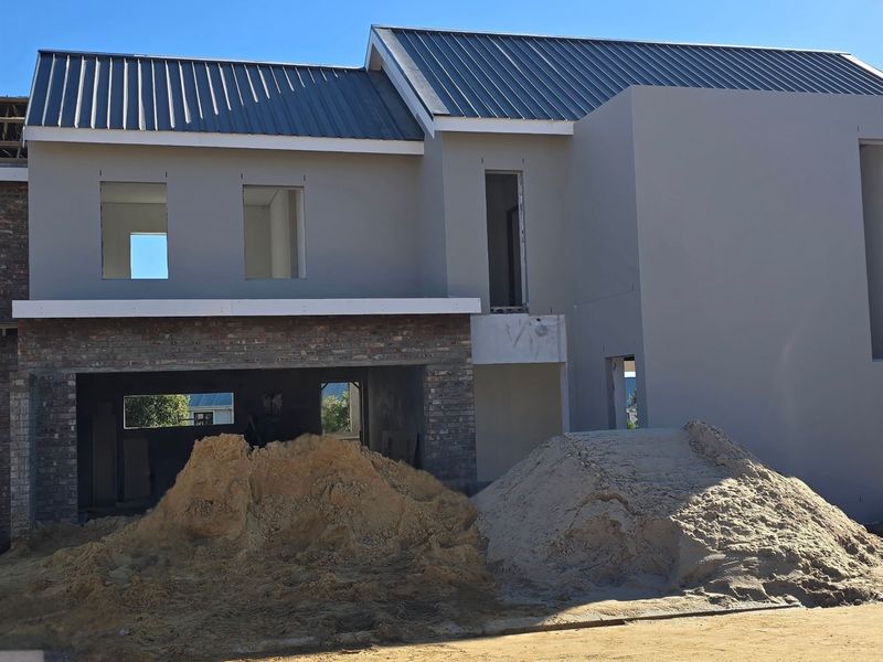 A front view of a residential property currently under construction, featuring a metal roof, brick and plastered exterior walls, and unfinished window openings.