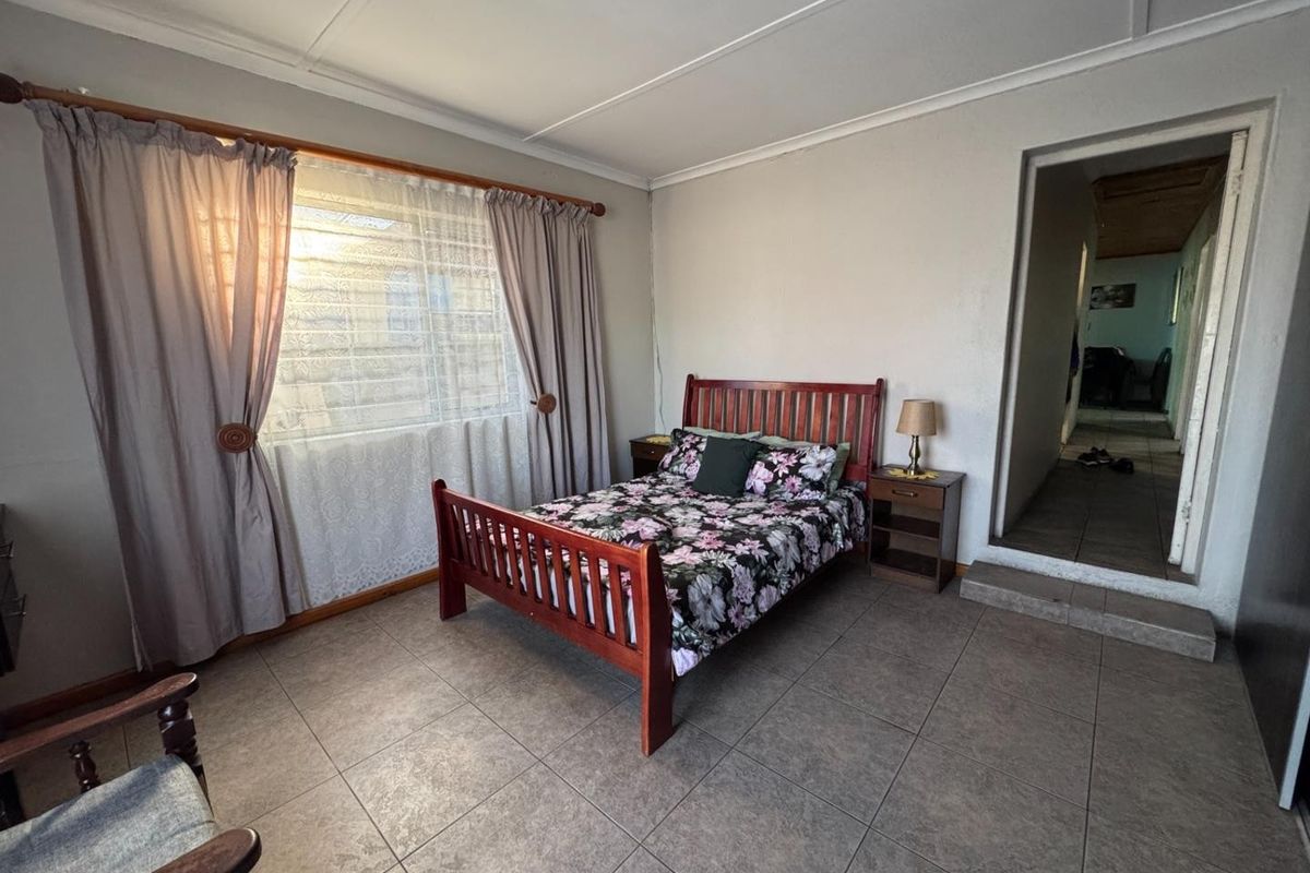 A bedroom featuring tiled flooring, a large window with curtain tracks, and a doorway leading to an adjacent room.