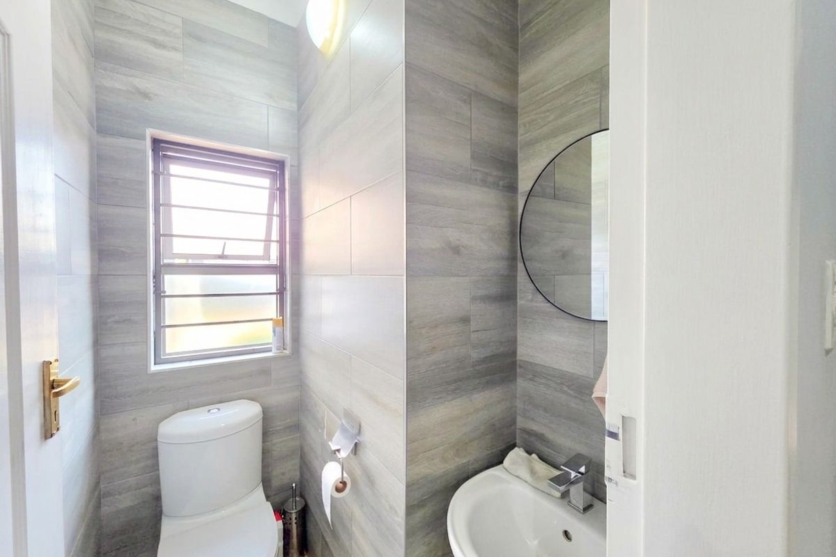 A compact, modern bathroom featuring grey wood-look wall tiles, a white toilet, and a small basin with a chrome mixer tap.