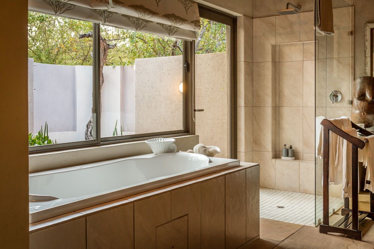A modern bathroom featuring a built-in bathtub, a spacious walk-in shower with a rain shower head, and neutral tiled finishes.