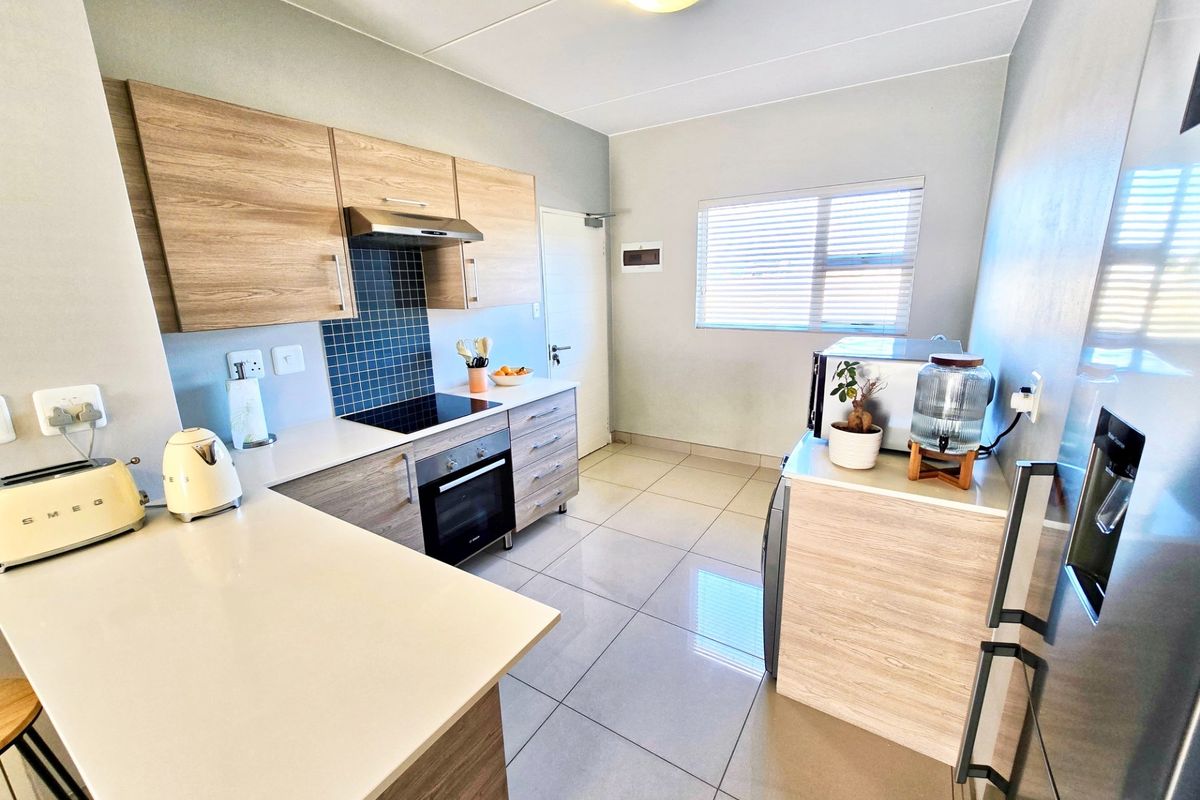 Modern kitchen featuring wood-grain cabinetry, stone-look countertops, a built-in oven with extractor fan, and tiled flooring throughout.