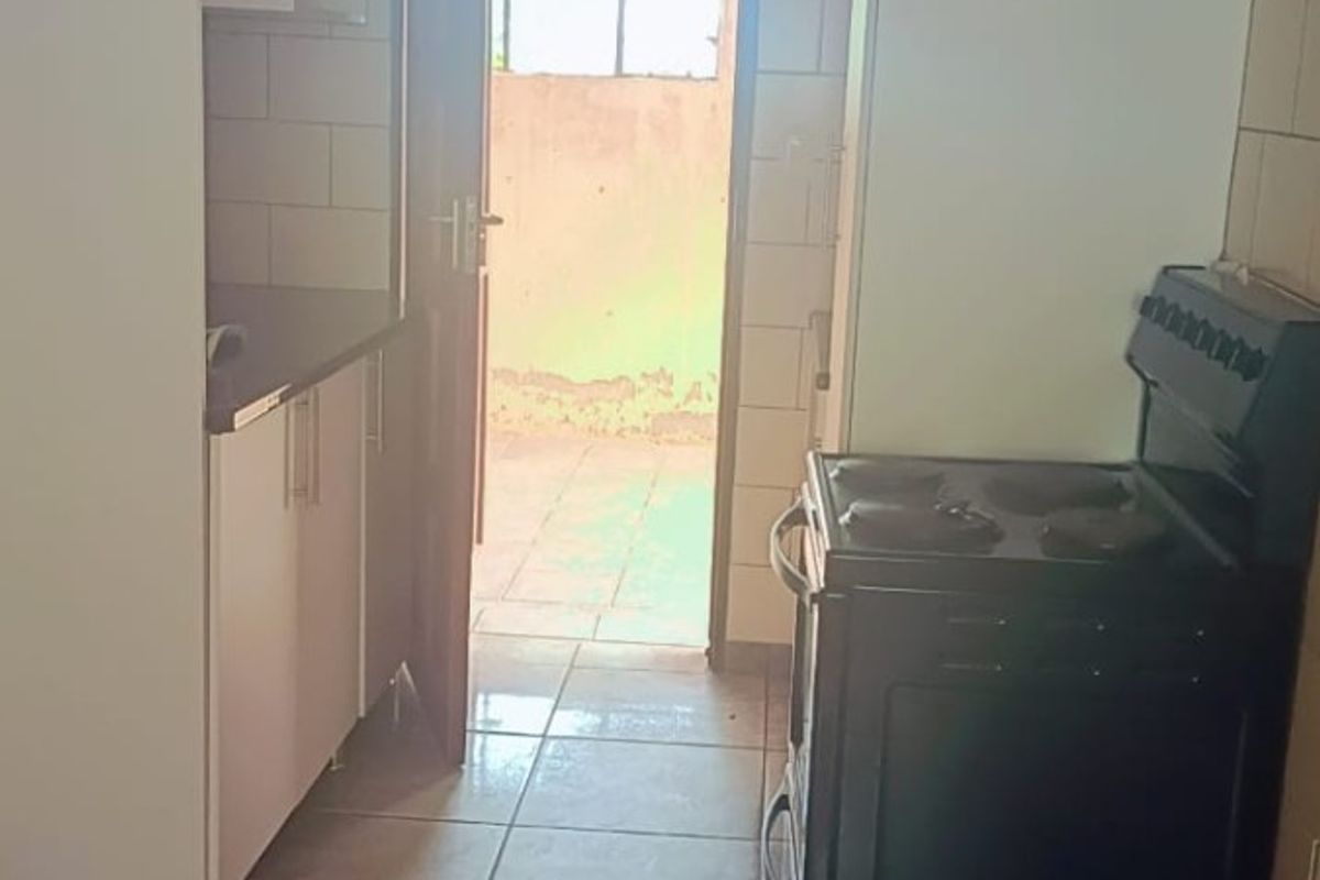 A functional kitchen featuring tiled flooring, white cabinetry, and a freestanding stove, with direct access to an outdoor area.