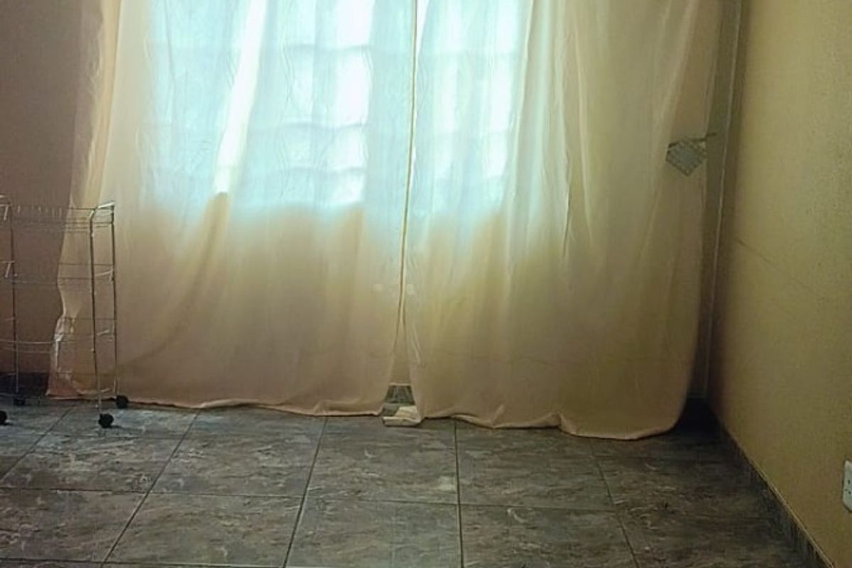 A simple bedroom or living area featuring tiled flooring and a large window covered by curtains.