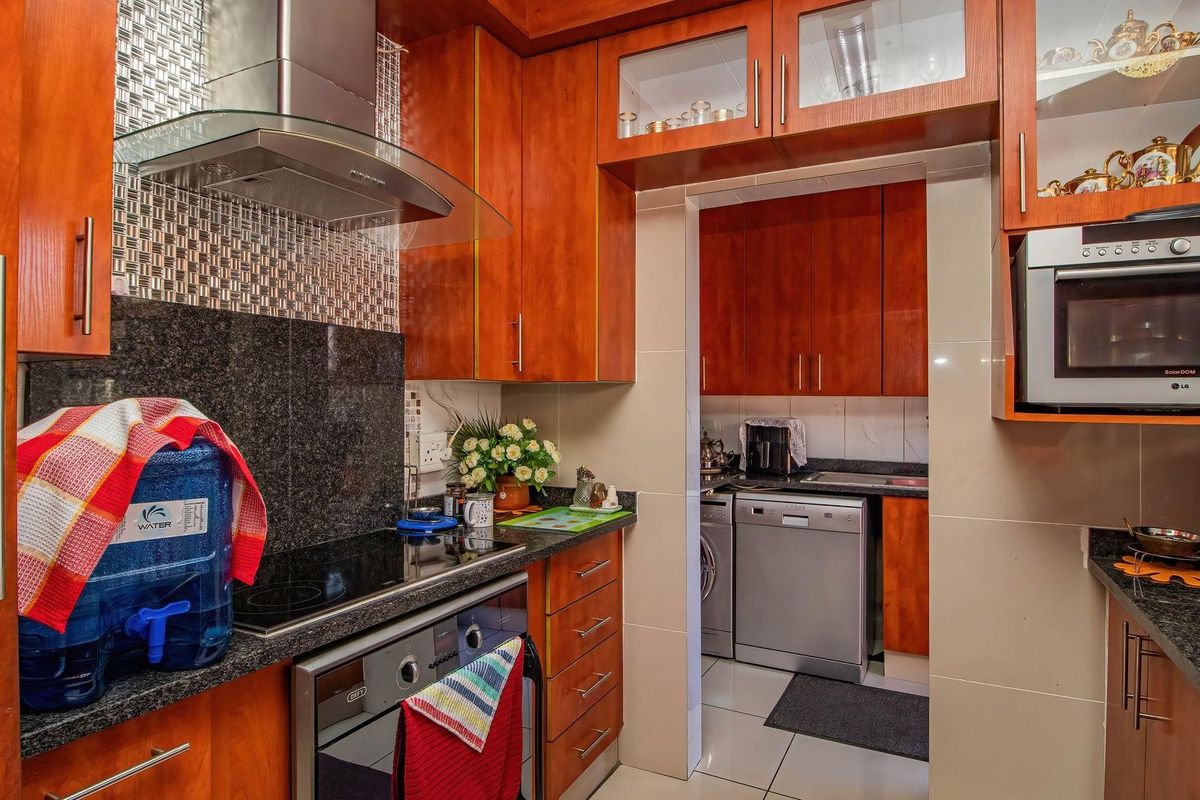 A functional kitchen featuring cherry wood cabinetry, granite countertops, a glass-top stove, and an integrated extractor fan, with an adjoining scullery area.