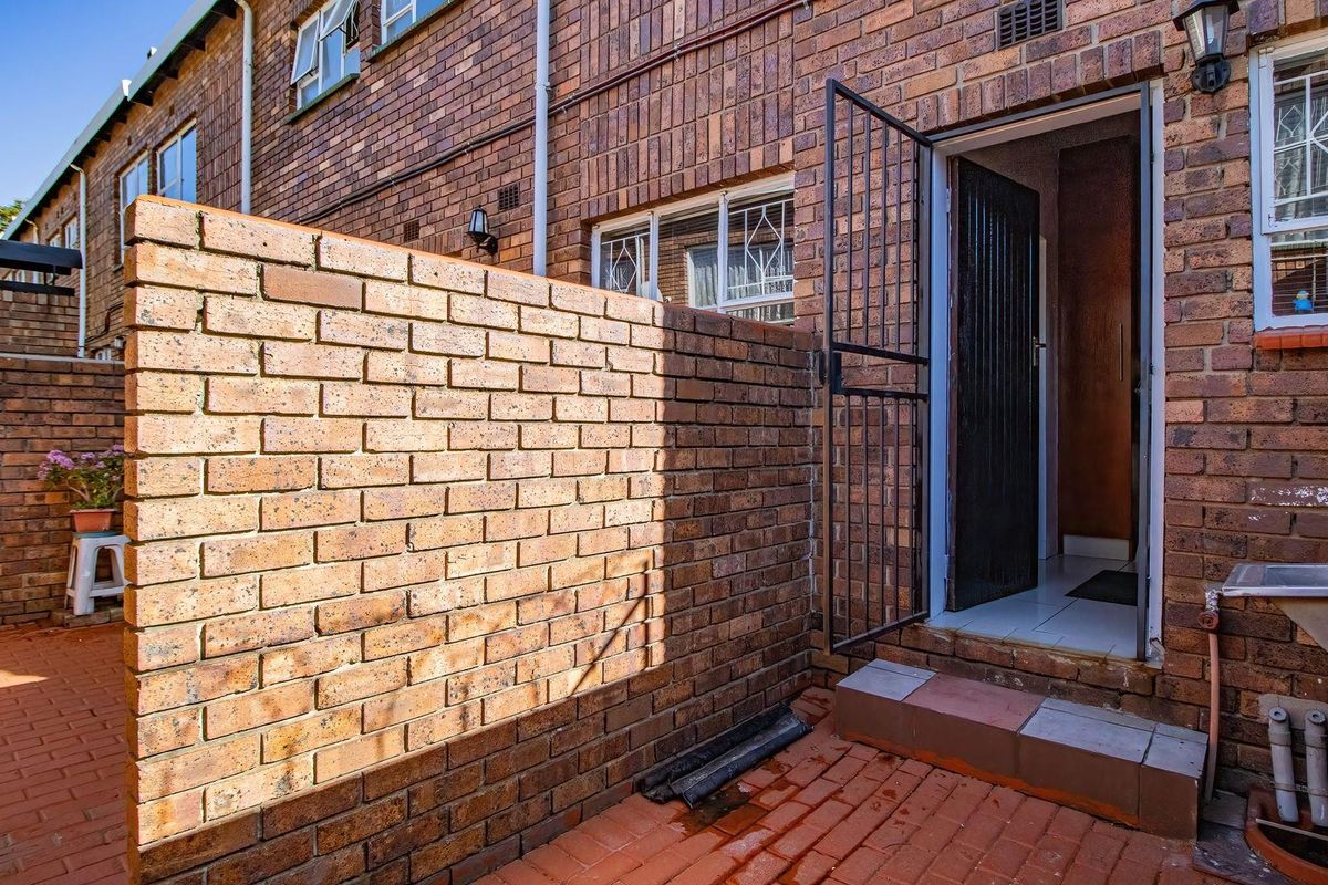A private rear courtyard featuring face-brick walls, paved flooring, a metal security gate, and an external utility sink.