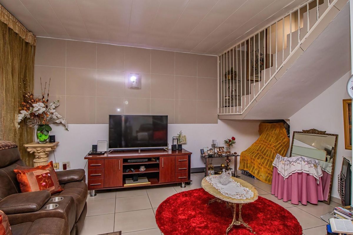 A living room area featuring tiled flooring, a staircase with a metal balustrade, and a tiled feature wall.