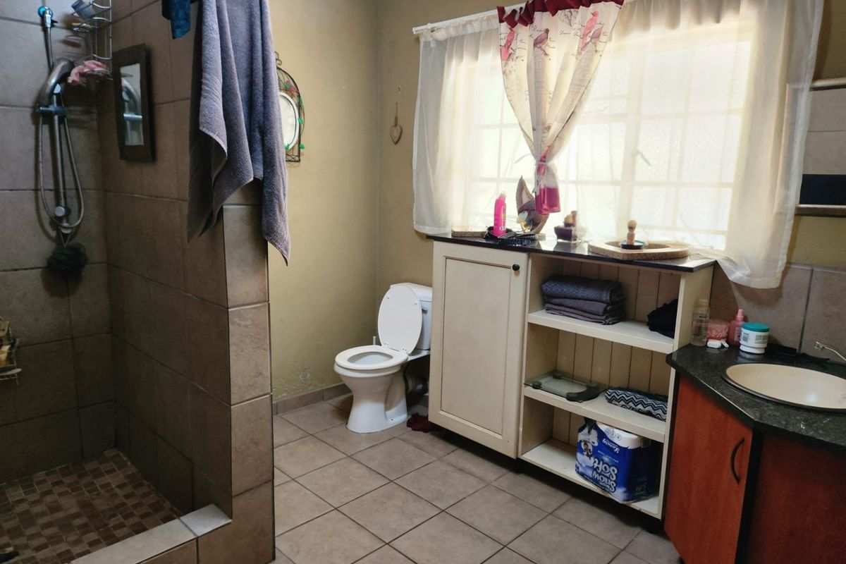 A functional bathroom featuring a walk-in shower, tiled flooring, a built-in vanity with storage, and a toilet.