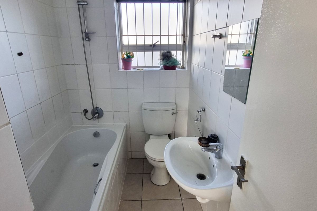 A functional bathroom featuring a bathtub with shower mixer, pedestal basin, and toilet, finished with white wall tiles and tiled flooring.