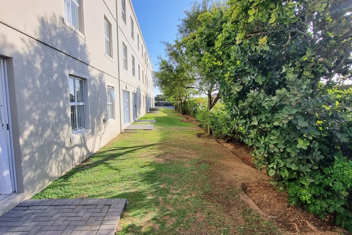 Rear exterior view of the apartment building featuring a paved walkway, sliding glass door access, and a landscaped garden area.