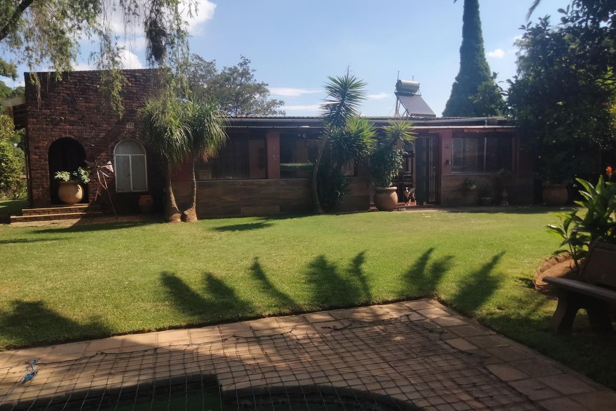 Rear view of the farm property featuring a brick facade, established garden, and a swimming pool area with a safety net.