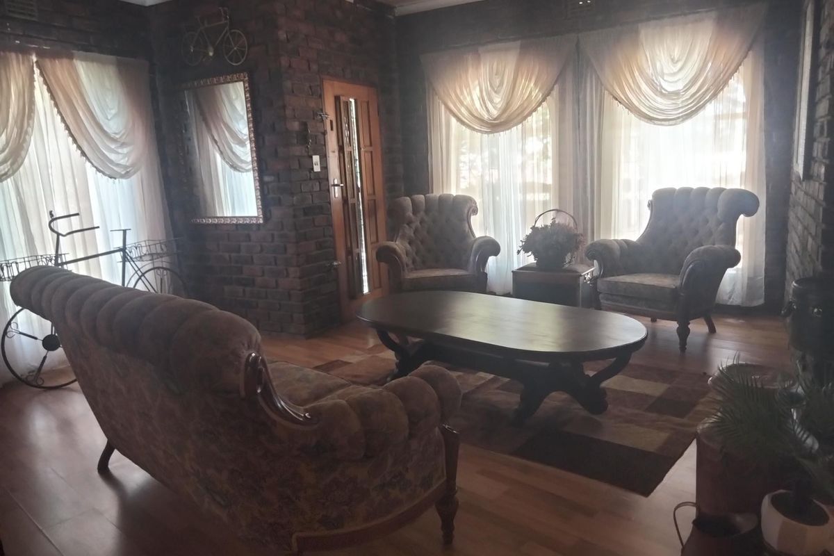 A cozy living room featuring exposed brick walls, laminate wood flooring, and large windows with draped curtains, creating a warm and traditional atmosphere.