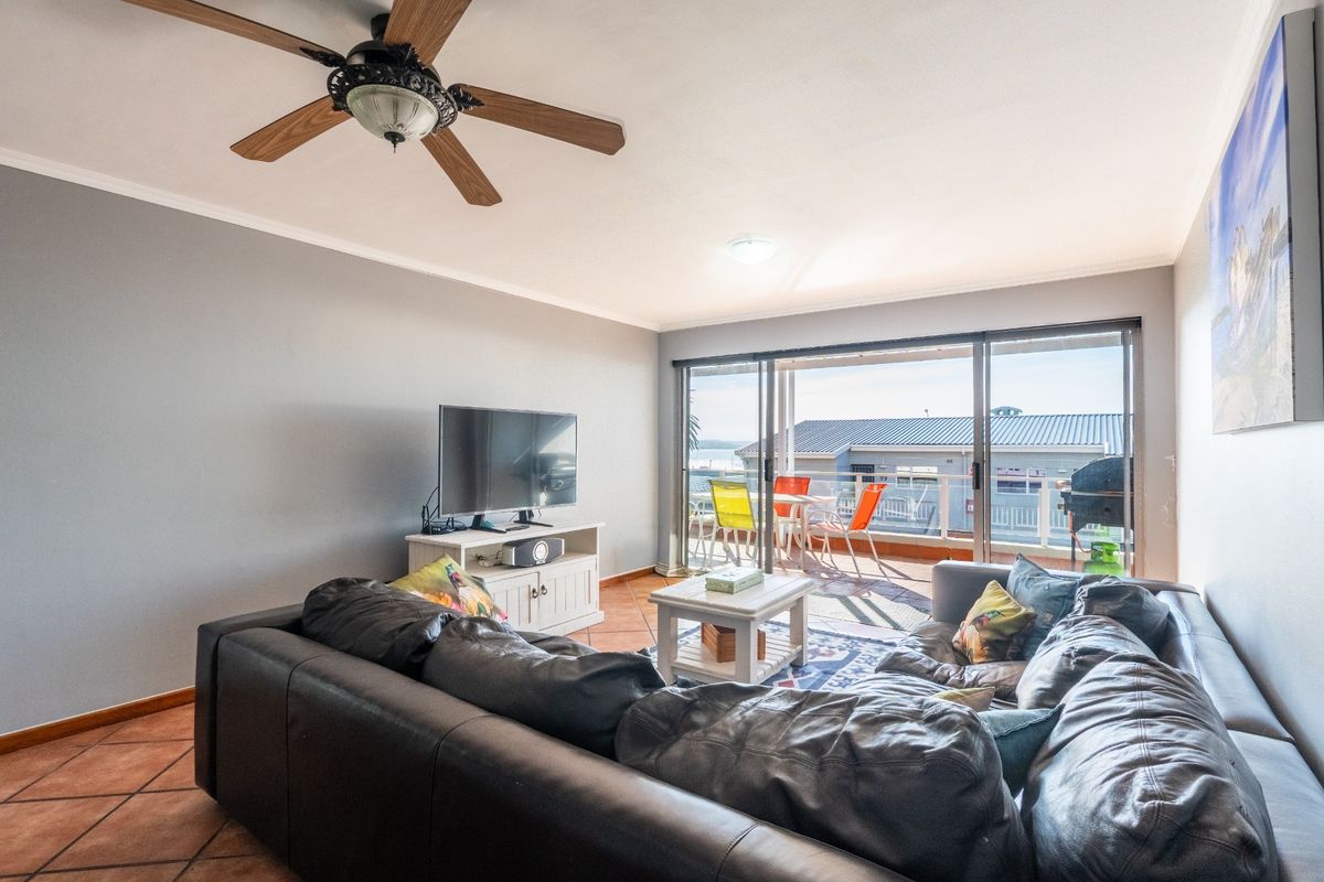 A comfortable living room featuring terracotta floor tiles, a ceiling fan, and large sliding glass doors that open onto a balcony with outdoor views.