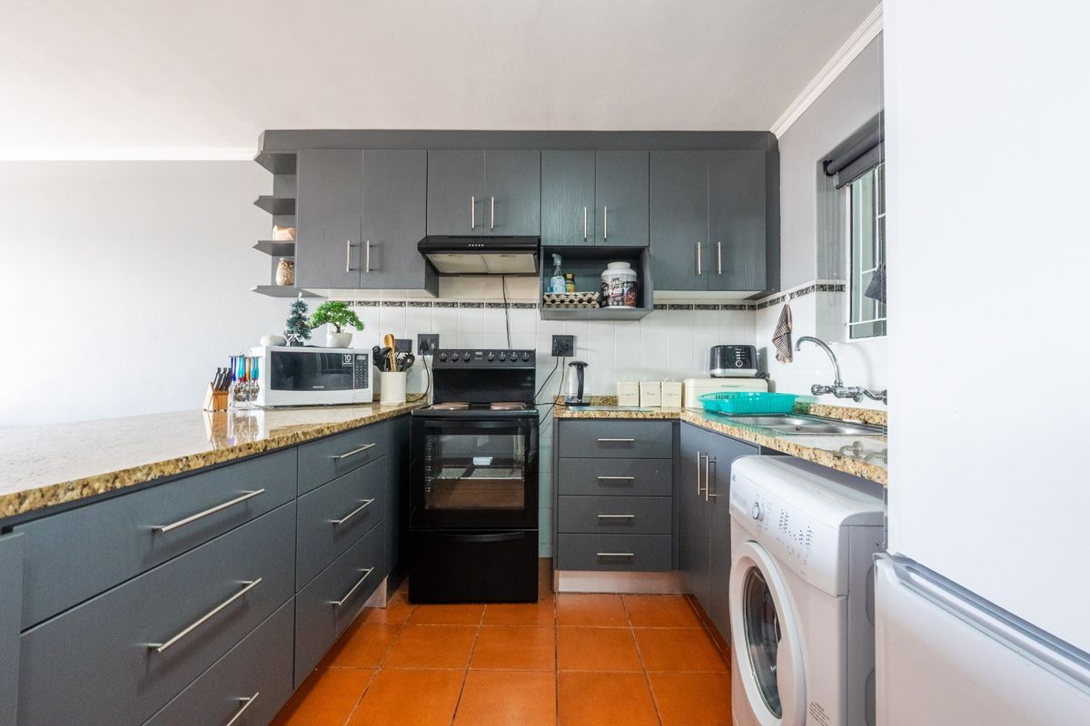 A functional kitchen featuring dark grey cabinetry, granite countertops, a built-in oven with extractor fan, and integrated plumbing for a washing machine.