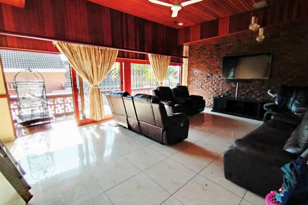 Spacious living room featuring a rustic exposed brick wall, high timber-paneled ceilings, and large sliding glass doors opening to an outdoor balcony area.