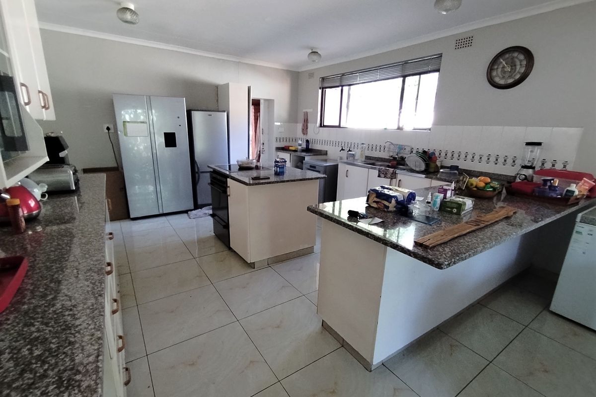 Spacious kitchen featuring granite countertops, a central island, tiled flooring, and ample cabinetry, providing a functional layout for meal preparation.