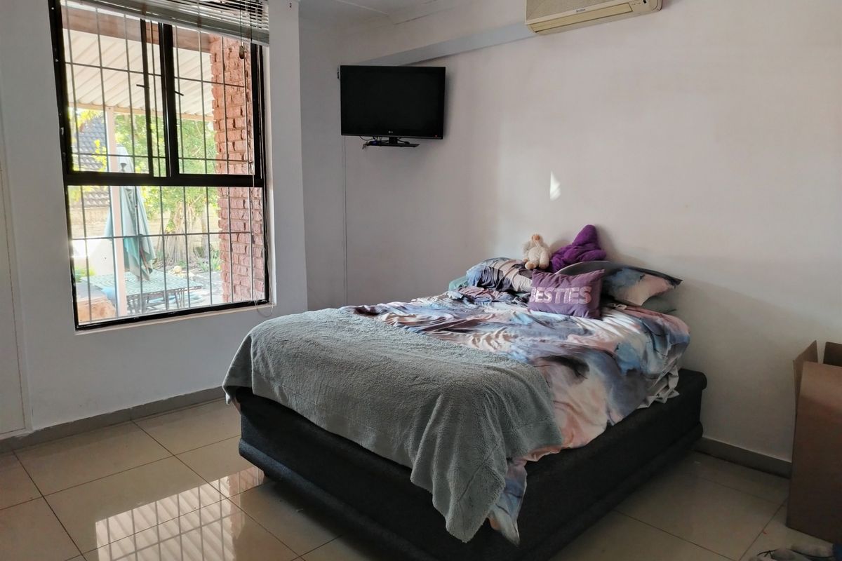 A bedroom featuring tiled flooring, a large window with security bars, and a wall-mounted air conditioning unit.