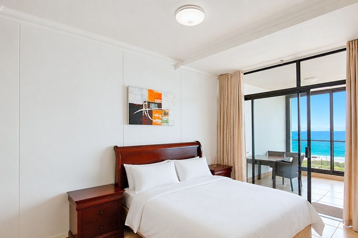 A bright bedroom featuring large sliding glass doors that open onto a private balcony with scenic ocean views.