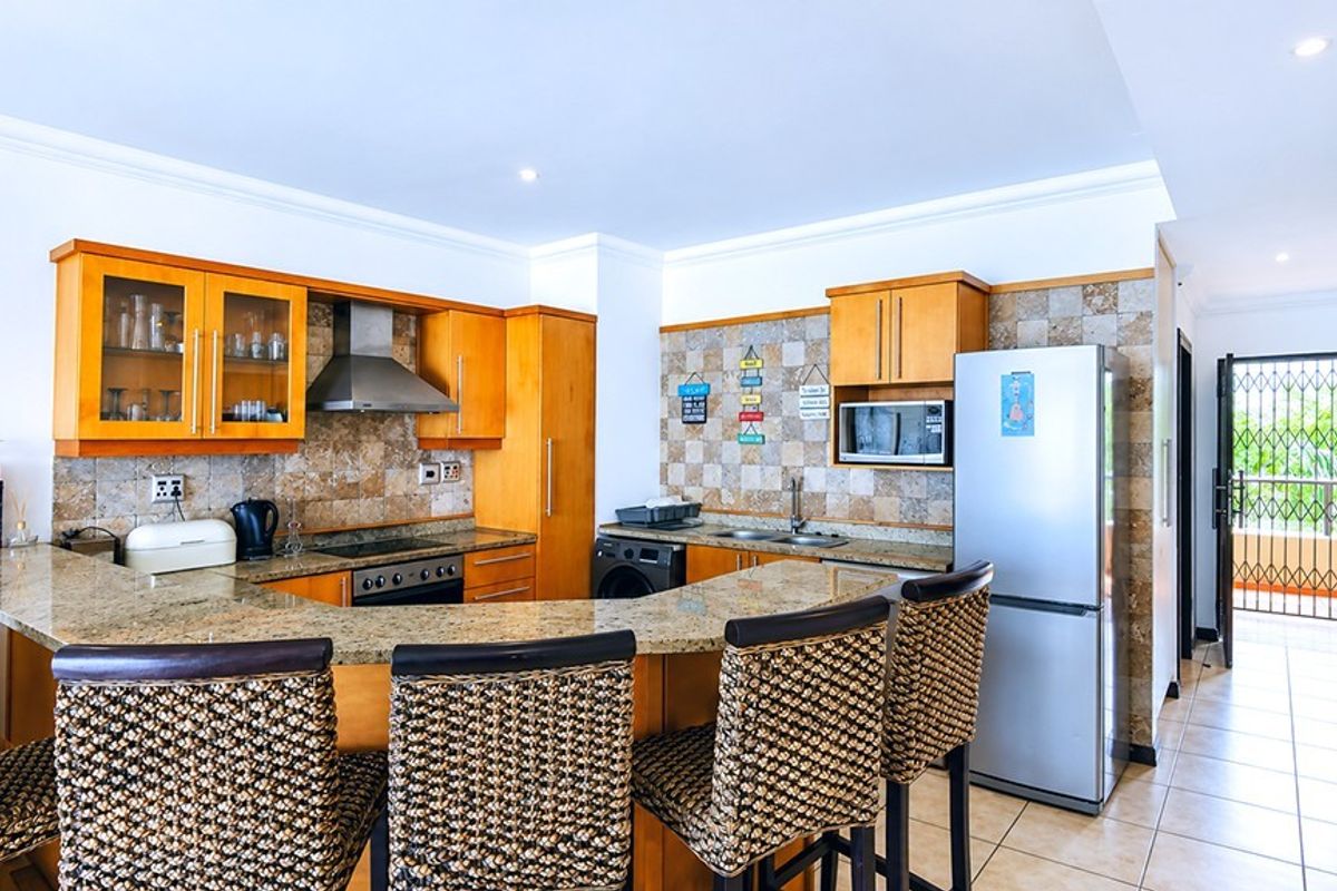 Kitchen featuring wooden cabinetry, granite countertops, a breakfast bar, tiled backsplash, and integrated stainless steel appliances, leading to an outdoor balcony area.