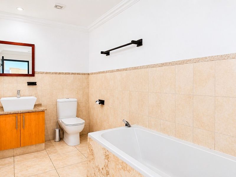 A well-maintained bathroom featuring a built-in vanity with a vessel sink, a standard toilet, and a tiled bathtub with wall-mounted fixtures.