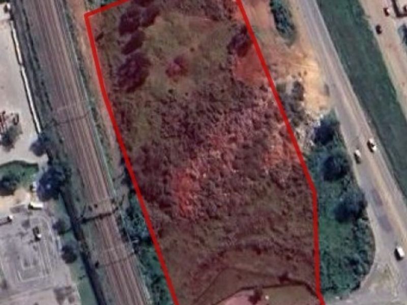 Aerial view of a vacant commercial land parcel with red boundary outline, situated near a railway line and main road access.