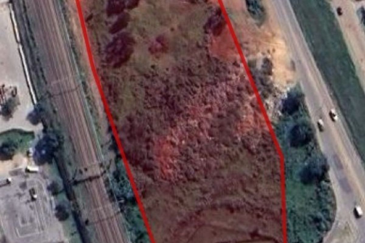 Aerial view of a vacant commercial land parcel with red boundary outline, situated near a railway line and main road access.