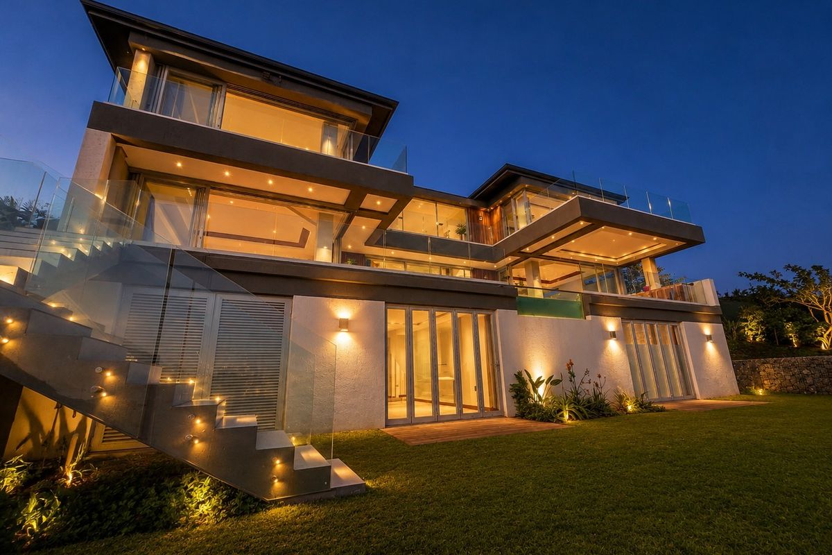 A stunning multi-level modern residence at dusk, featuring expansive glass balconies, integrated exterior lighting, and a beautifully landscaped garden.
